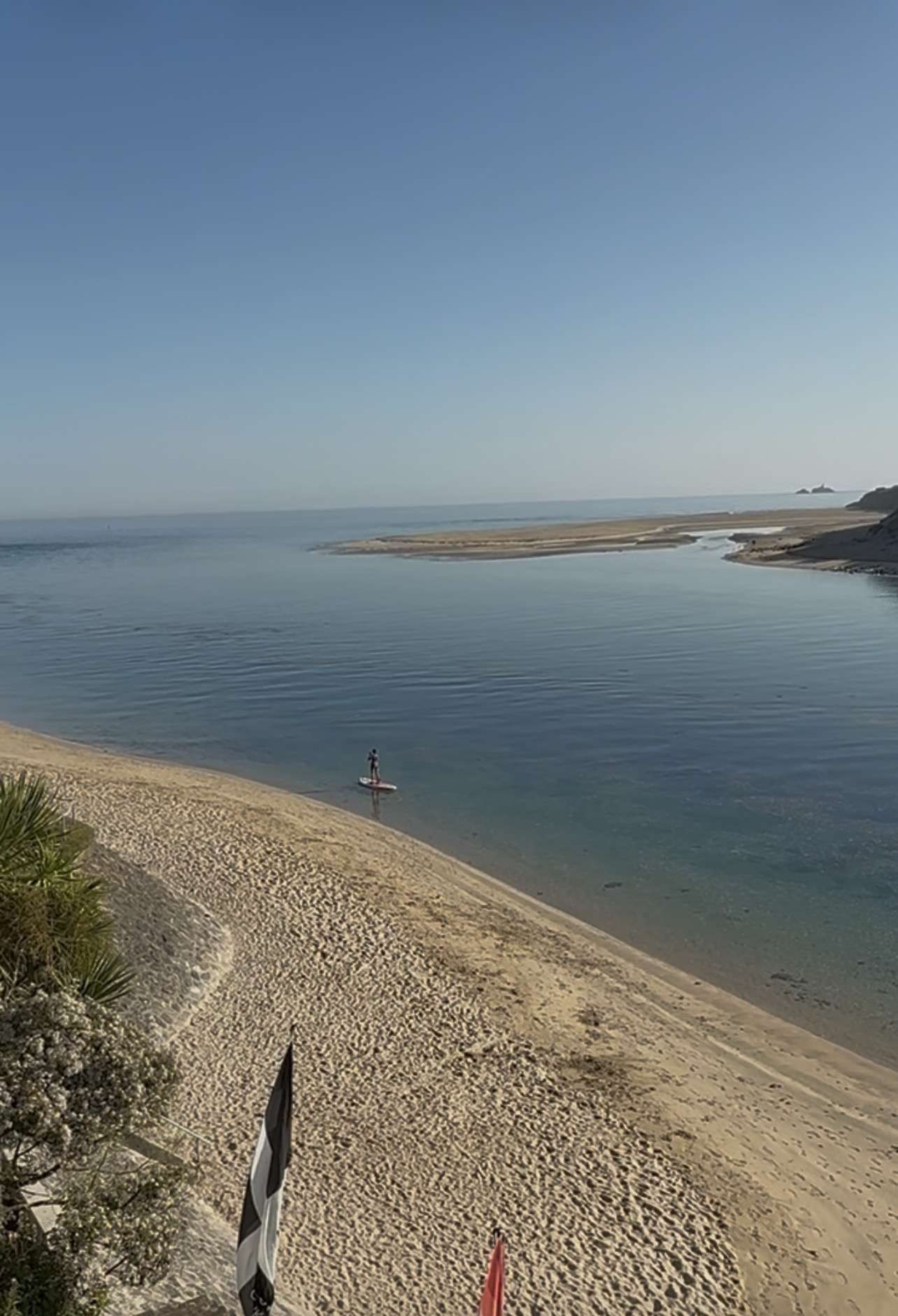 Loan Paddleboarder on calm blue sea by a golden sandy beach
