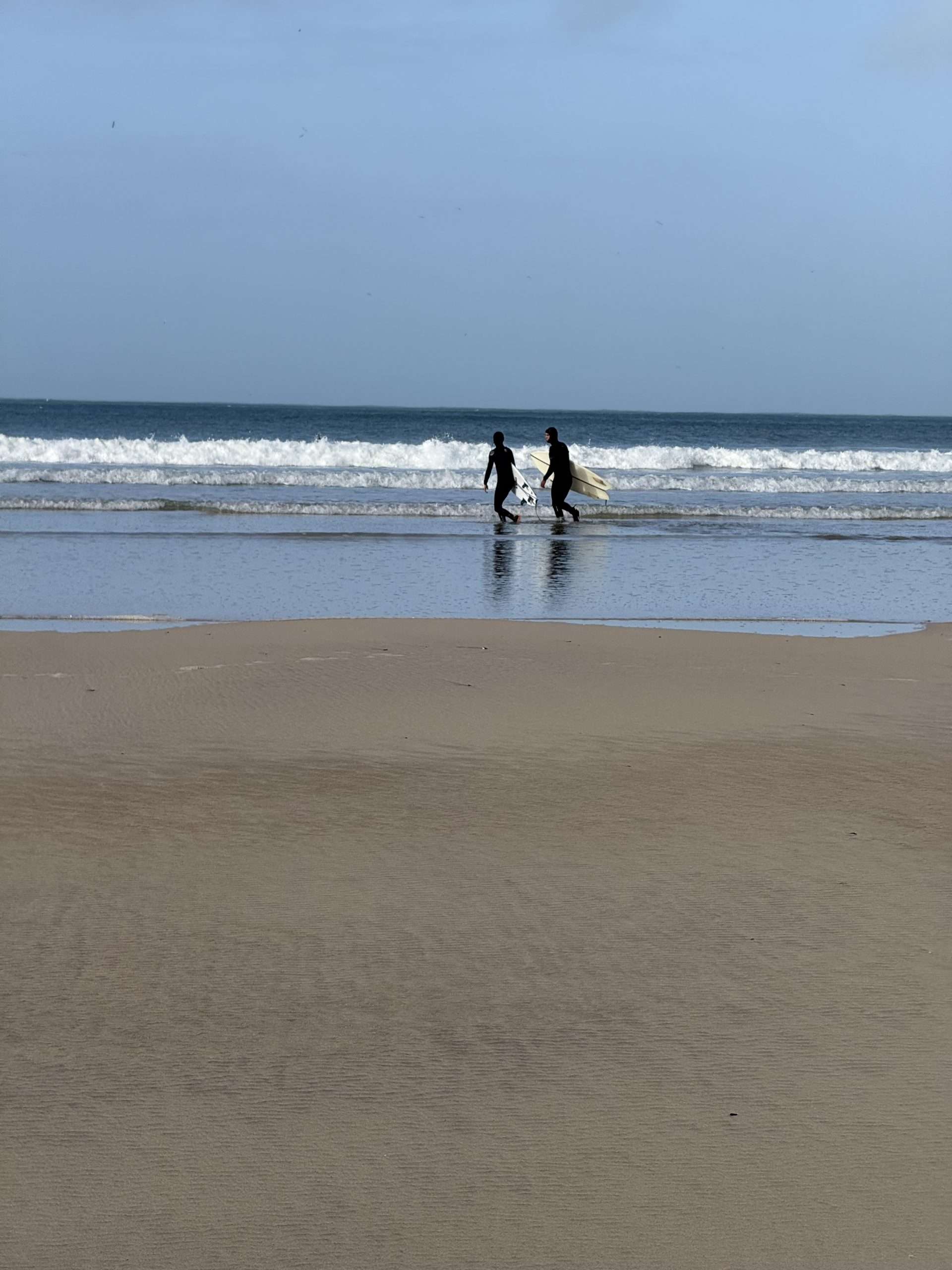 Two Surfers carrying surf boards walking into the sea