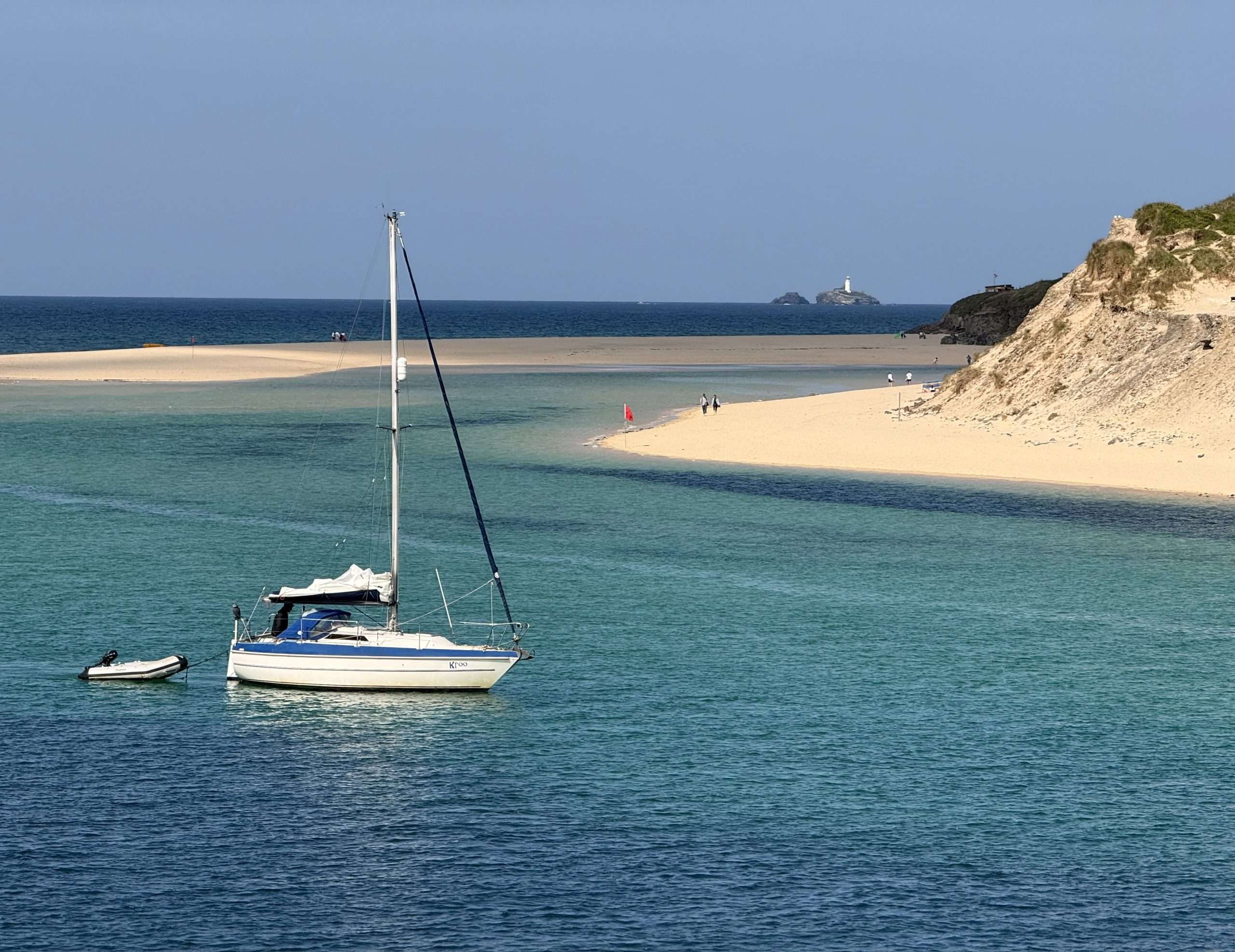 Sailboat on calm turquoise water with golden sand in the foreground.
